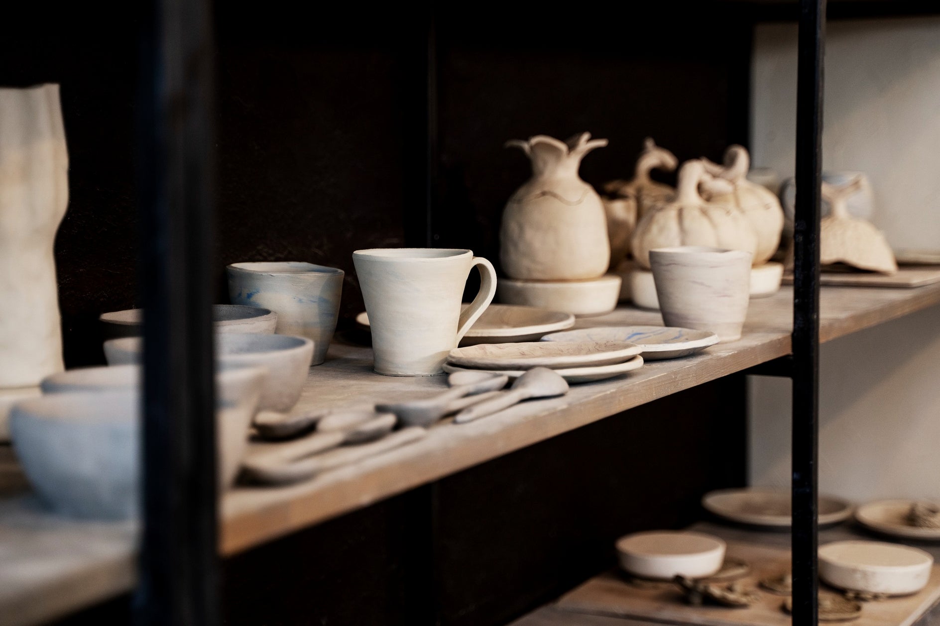 Display of ceramicware including cups, bowls, and vases on a wooden shelf.