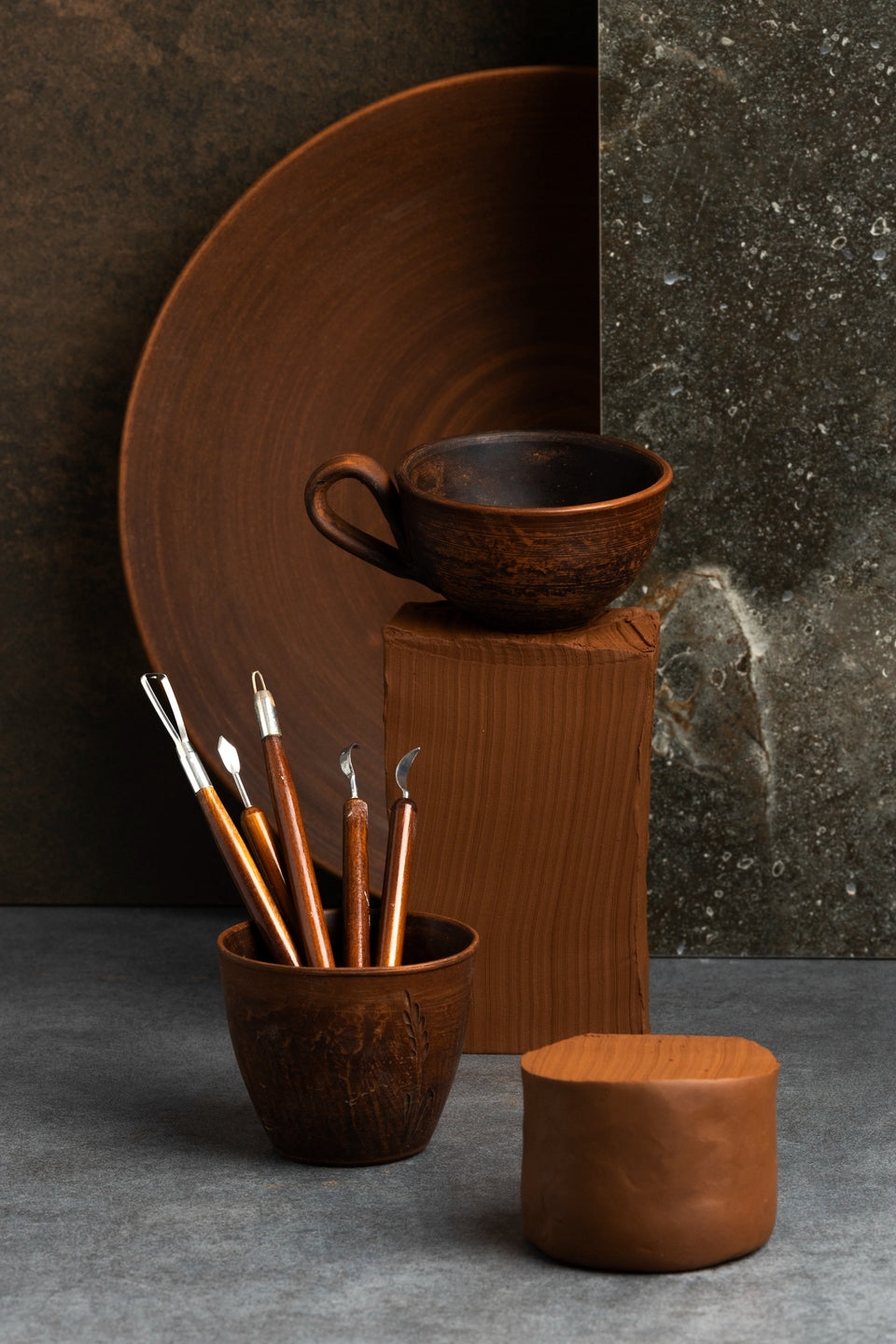 Brown ceramic items including a cup, plate, and small container on a dark background