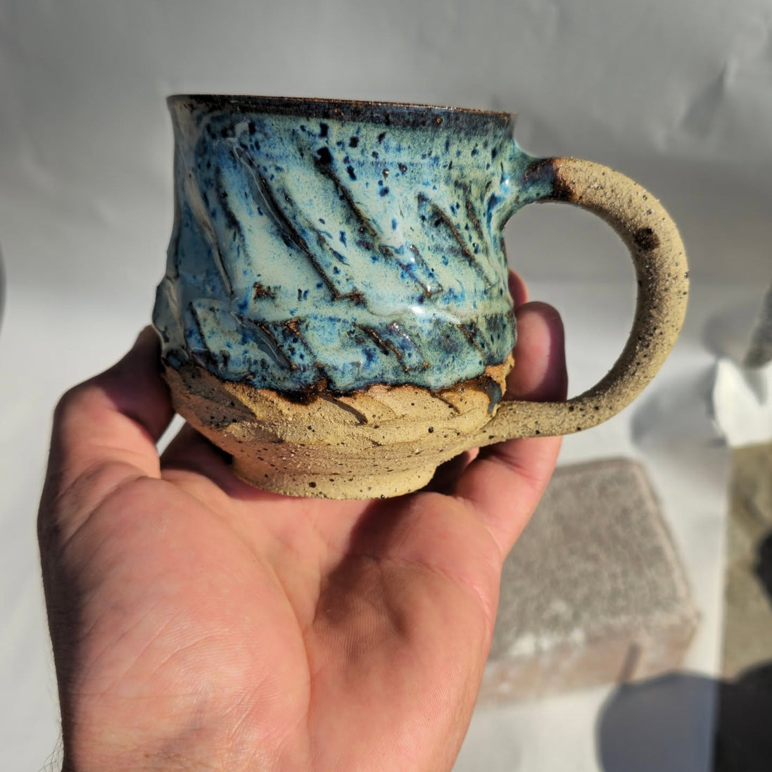 Hand holding a ceramic mug with blue and brown glaze against a neutral background