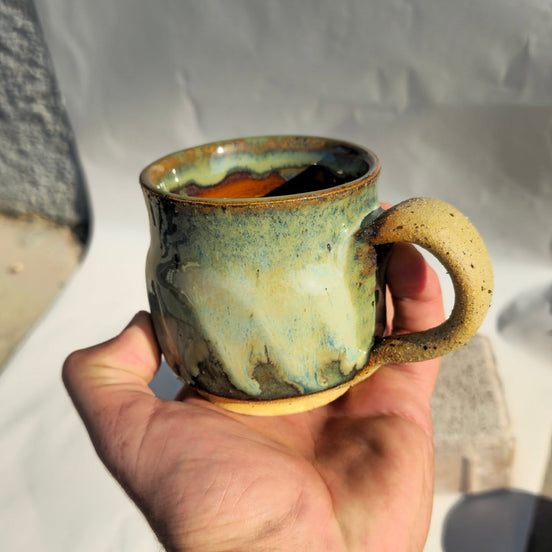 Hand holding a ceramic mug with a textured surface against a neutral background
