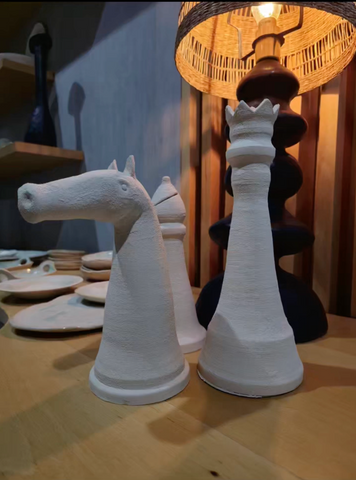 3D-printed chess pieces on a wooden table with a lamp in the background