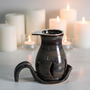 Black ceramic oil burner with a tray on a white surface with lit candles in the background