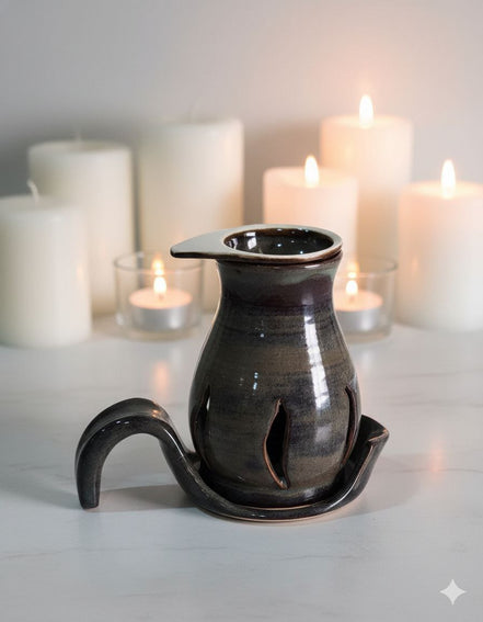 Black ceramic oil burner with a tray on a white surface with lit candles in the background
