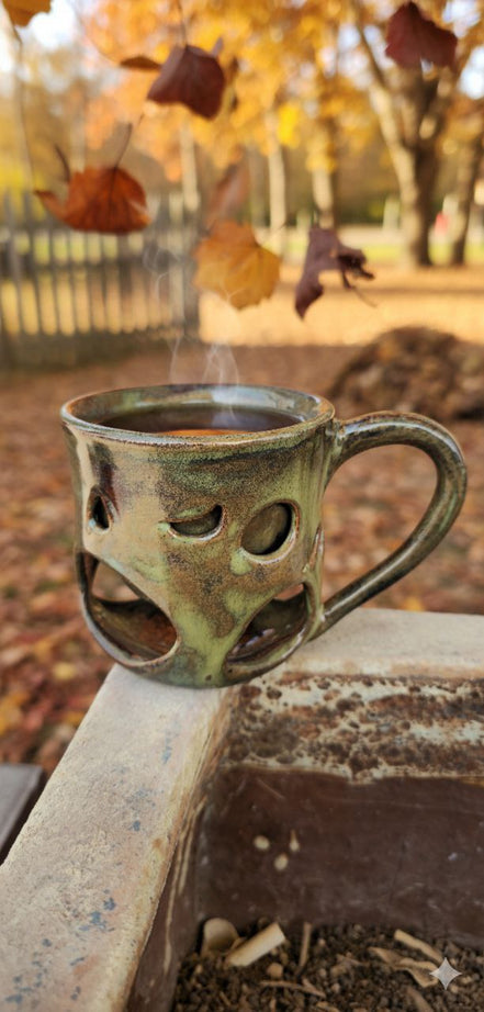 Steaming mug with decorative cut-out design on a stone ledge with autumn leaves in the background