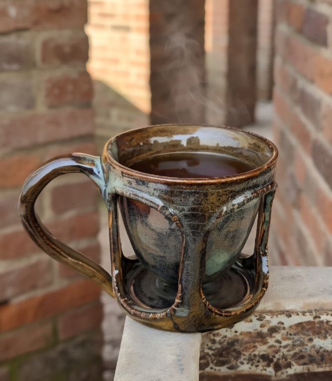 Ceramic mug with a handle, filled with a dark liquid, against a brick wall.