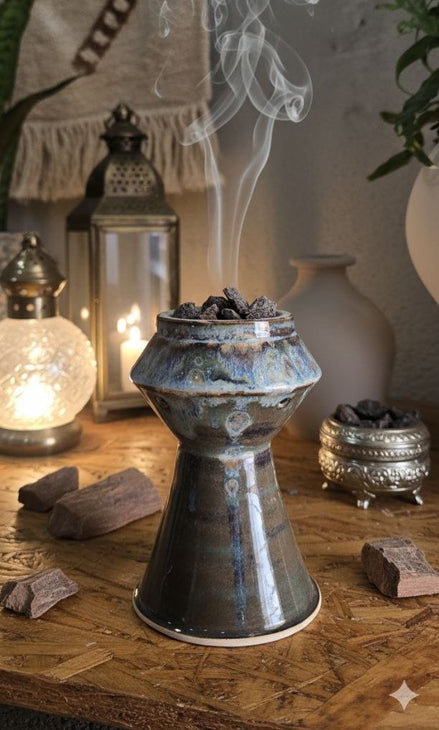 Ceramic incense burner with smoke on a wooden surface with lanterns and incense sticks.