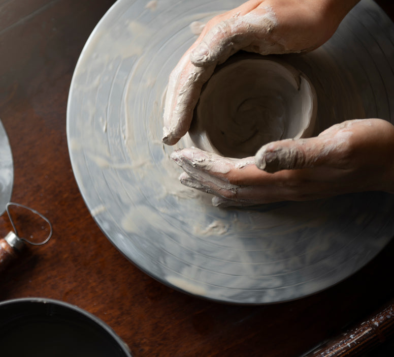 Person shaping a pot on a pottery wheel with clay on hands